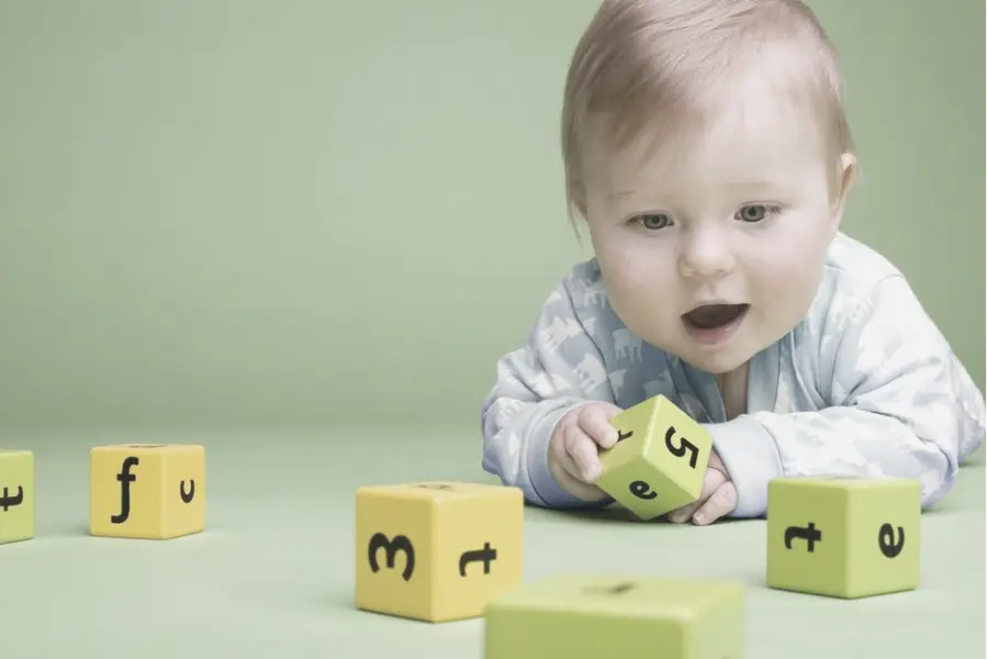 Foto eines Säuglings, der auf dem Bauch liegt und aufmerksam einen grünen Spielzeugwürfel mit Zahlen betrachtet – Entwicklungssprünge und Babyschlaf